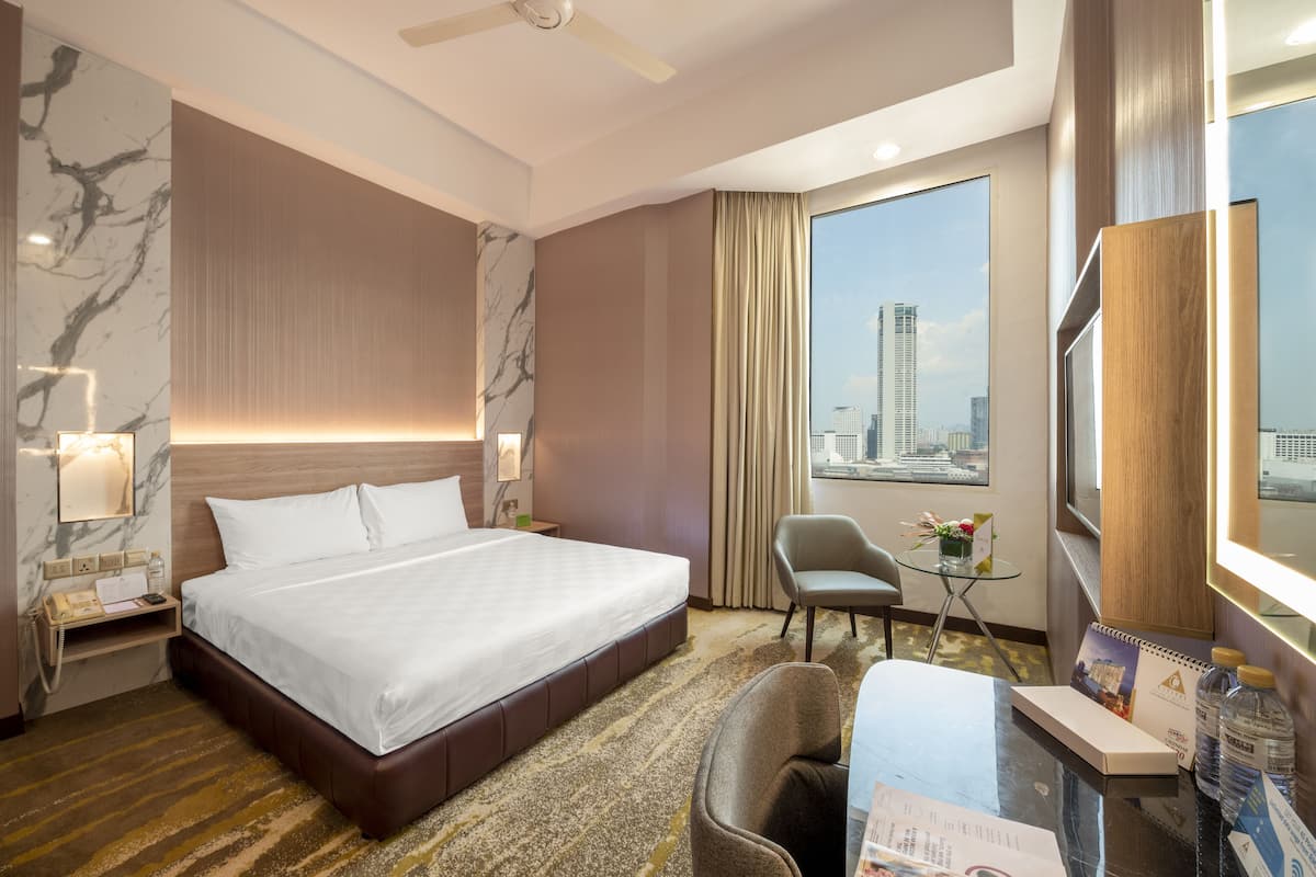A hotel room with a large bed, a desk with a chair, a small table with a plant, and a city view through the window.