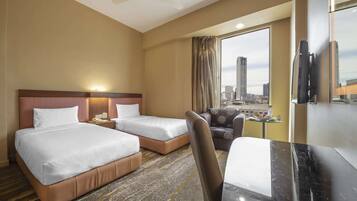 A hotel room with two beds, a desk, a chair, a television, and a large window with a city view.