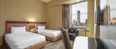 A hotel room with two beds, a desk, a chair, a television, and a large window with a city view.