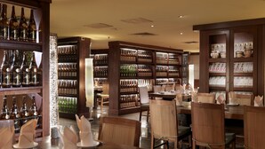Un restaurante con mesas y sillas de madera, estantes llenos de botellas y una pared decorativa.
