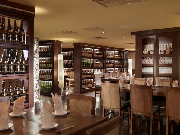 Un restaurante con mesas y sillas de madera, estantes llenos de botellas y una pared decorativa.