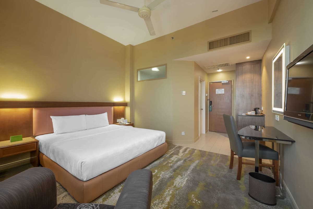A hotel room with a large bed, a desk, a chair, a TV, and a bathroom visible through an open door.