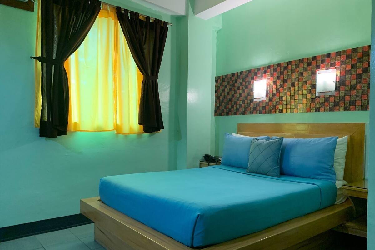 A room with a bed, a nightstand, a telephone, and a window with curtains.