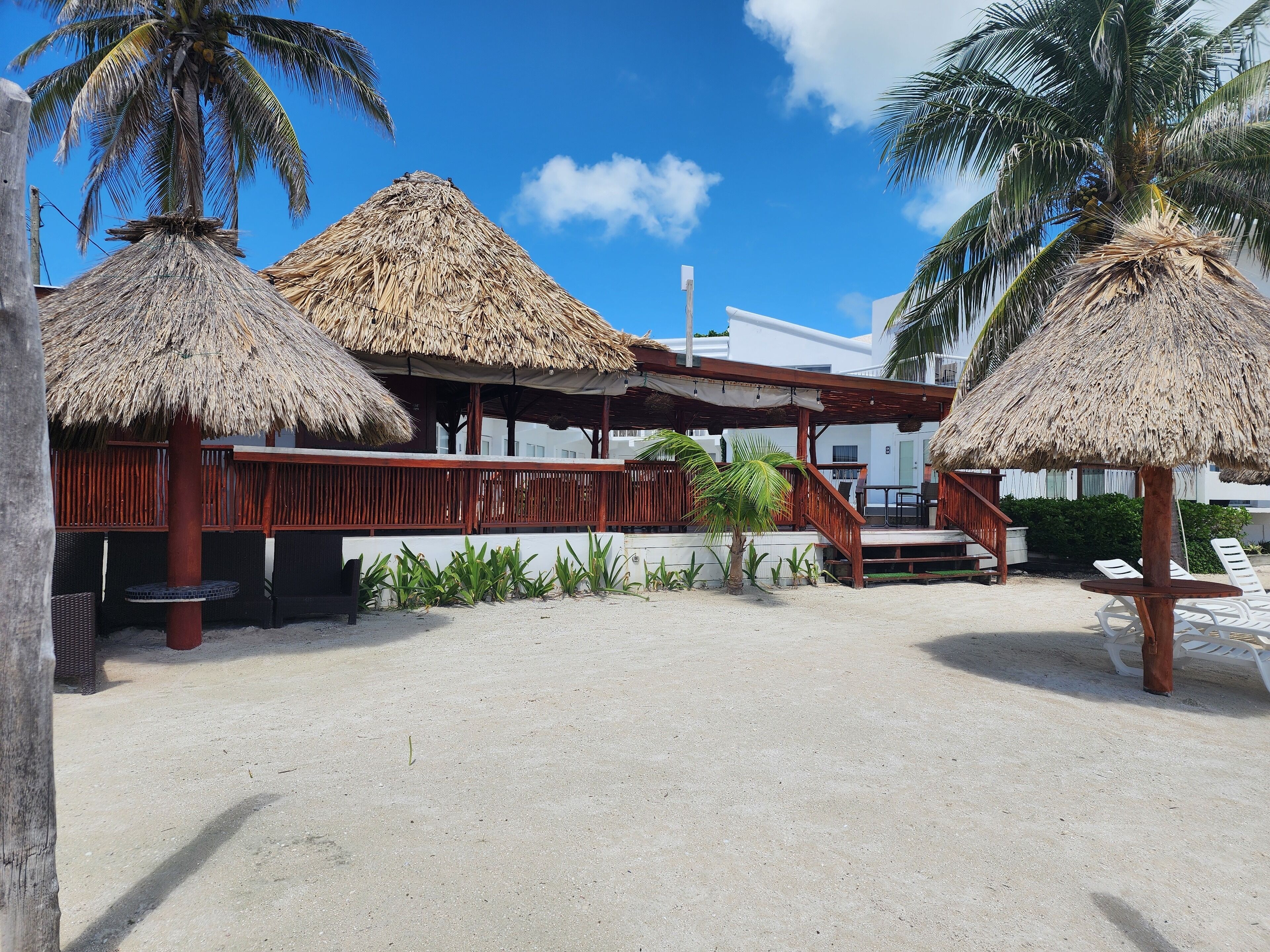 A beachside resort with thatched-roof structures, a wooden deck, and lounge chairs.