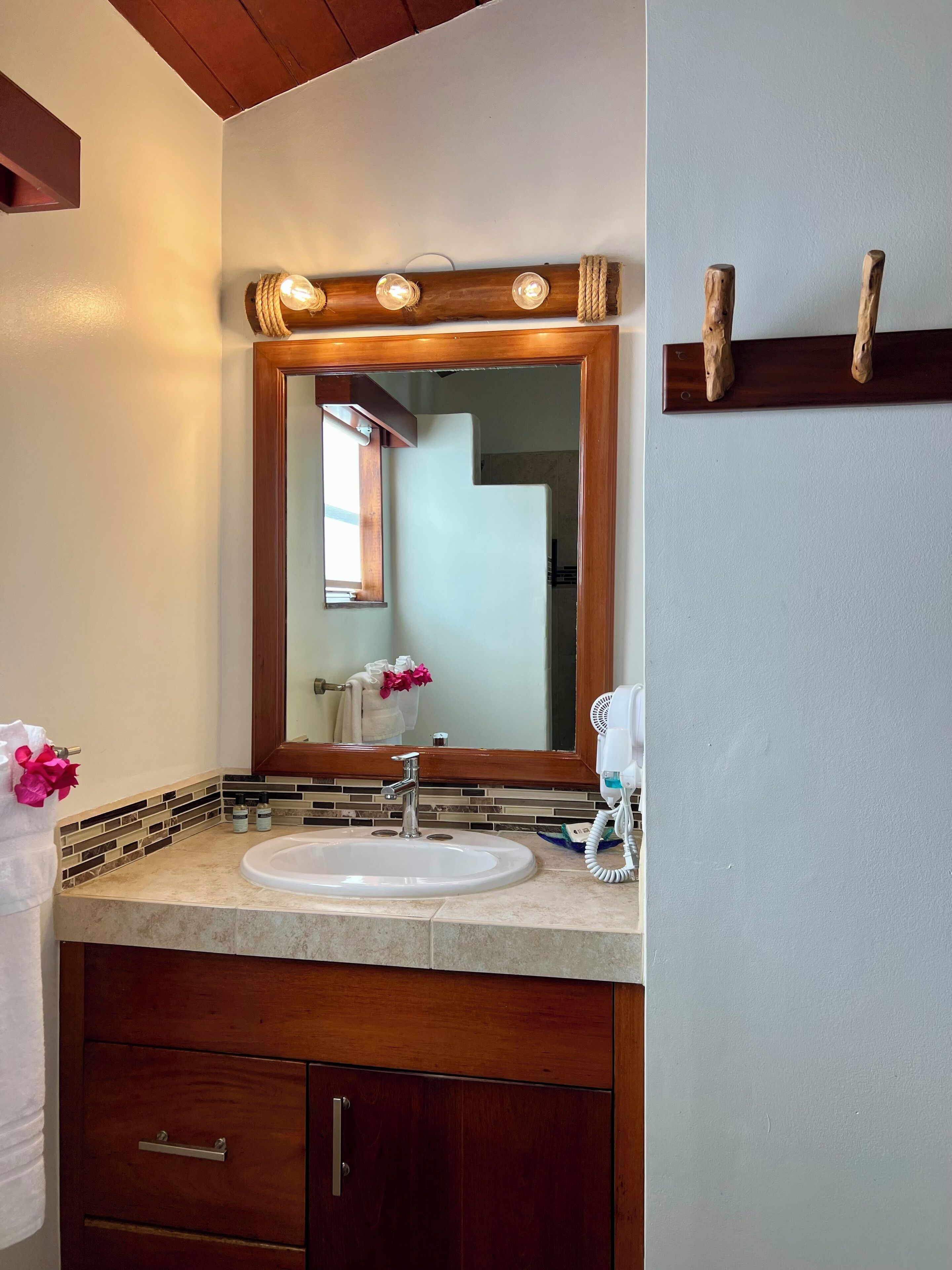 A bathroom with a large mirror, a sink, and a vanity with drawers. There are lights above the mirror and a towel rack on the wall.