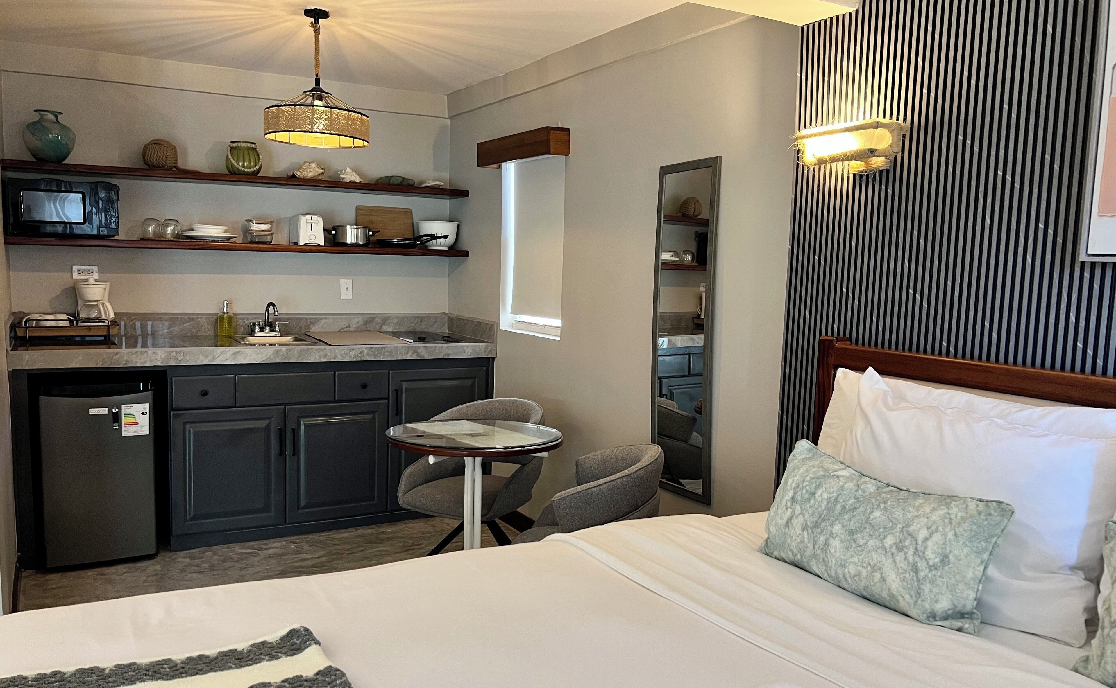 Een kleine hotelkamer met kitchenette, een eettafeltje, een enkel bed met kussen en een spiegel.