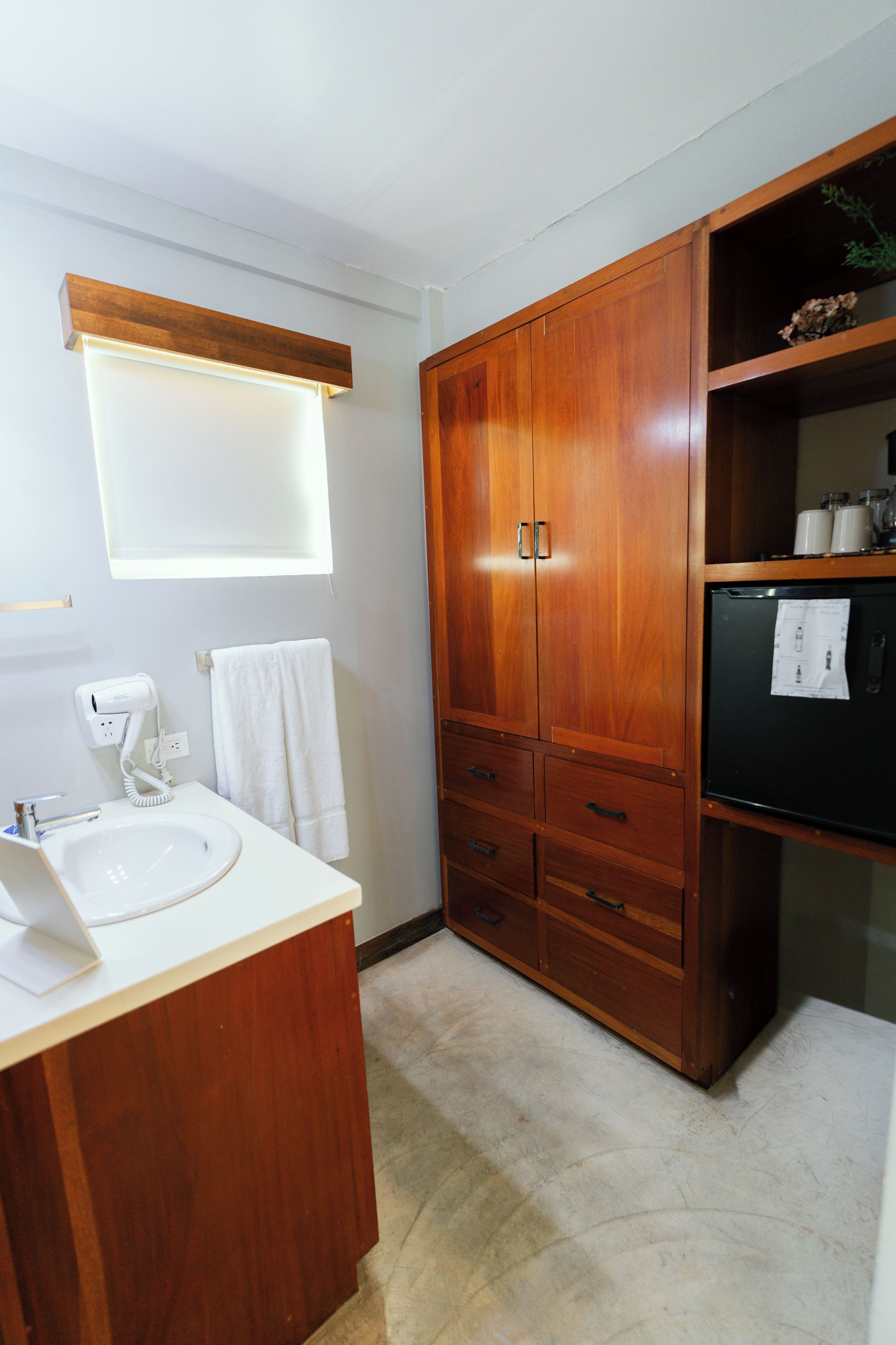 Een badkamer met een houten wastafelmeubel, een witte wastafel, een haardroger en een handdoek aan de muur.