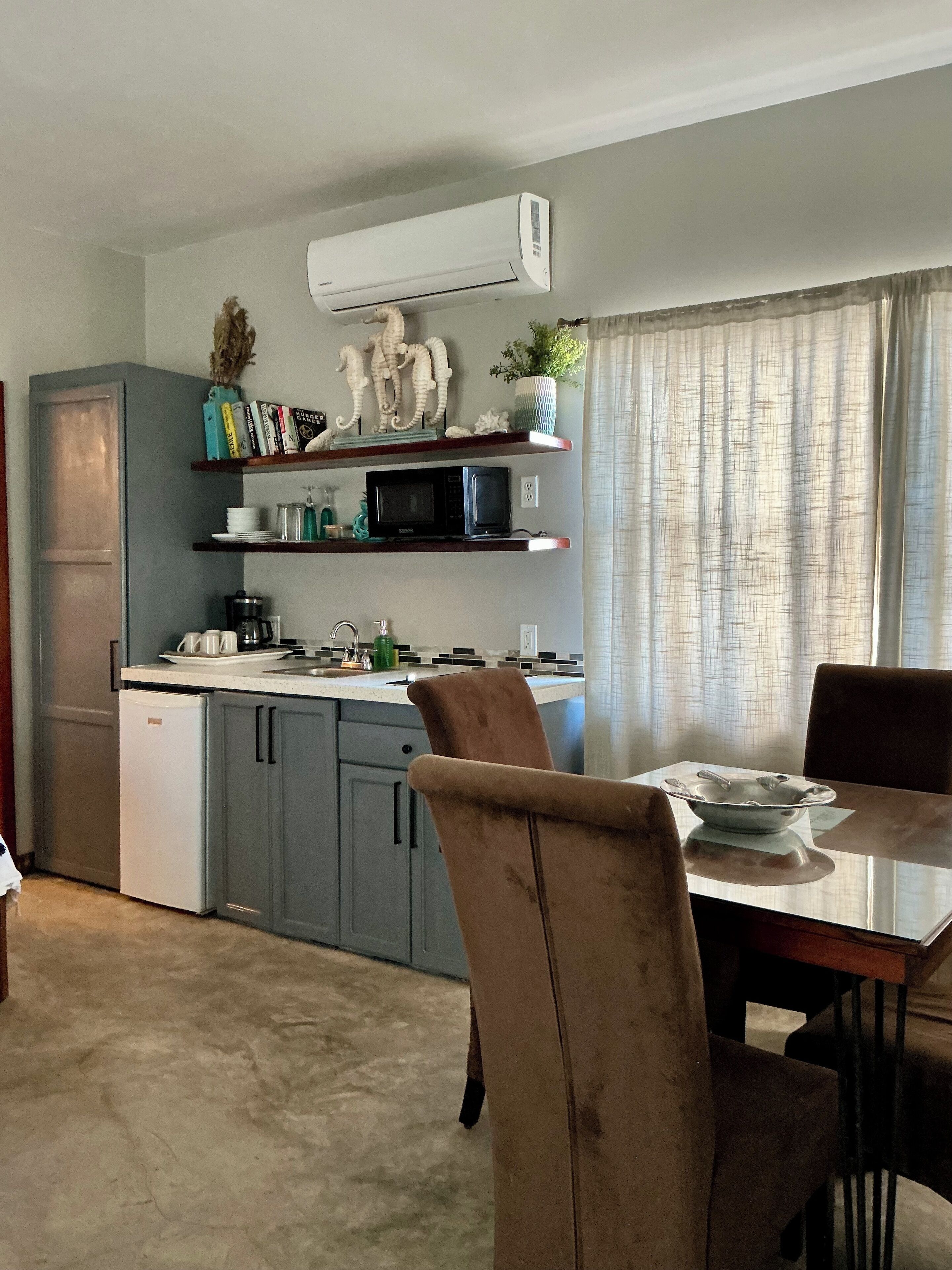 A compact kitchen with a microwave, stove, and sink. There is a dining table with chairs and a small refrigerator.