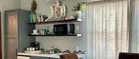 A compact kitchen with a microwave, stove, and sink. There is a dining table with chairs and a small refrigerator.