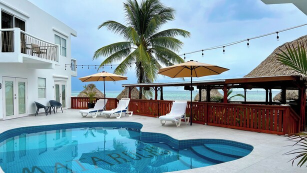 A pool area with lounge chairs and umbrellas, a view of the ocean, and a building with a balcony.