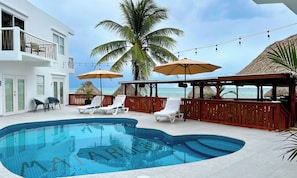 A pool area with lounge chairs and umbrellas, a view of the ocean, and a building with a balcony. - Mata Rocks Resort (San Pedro)