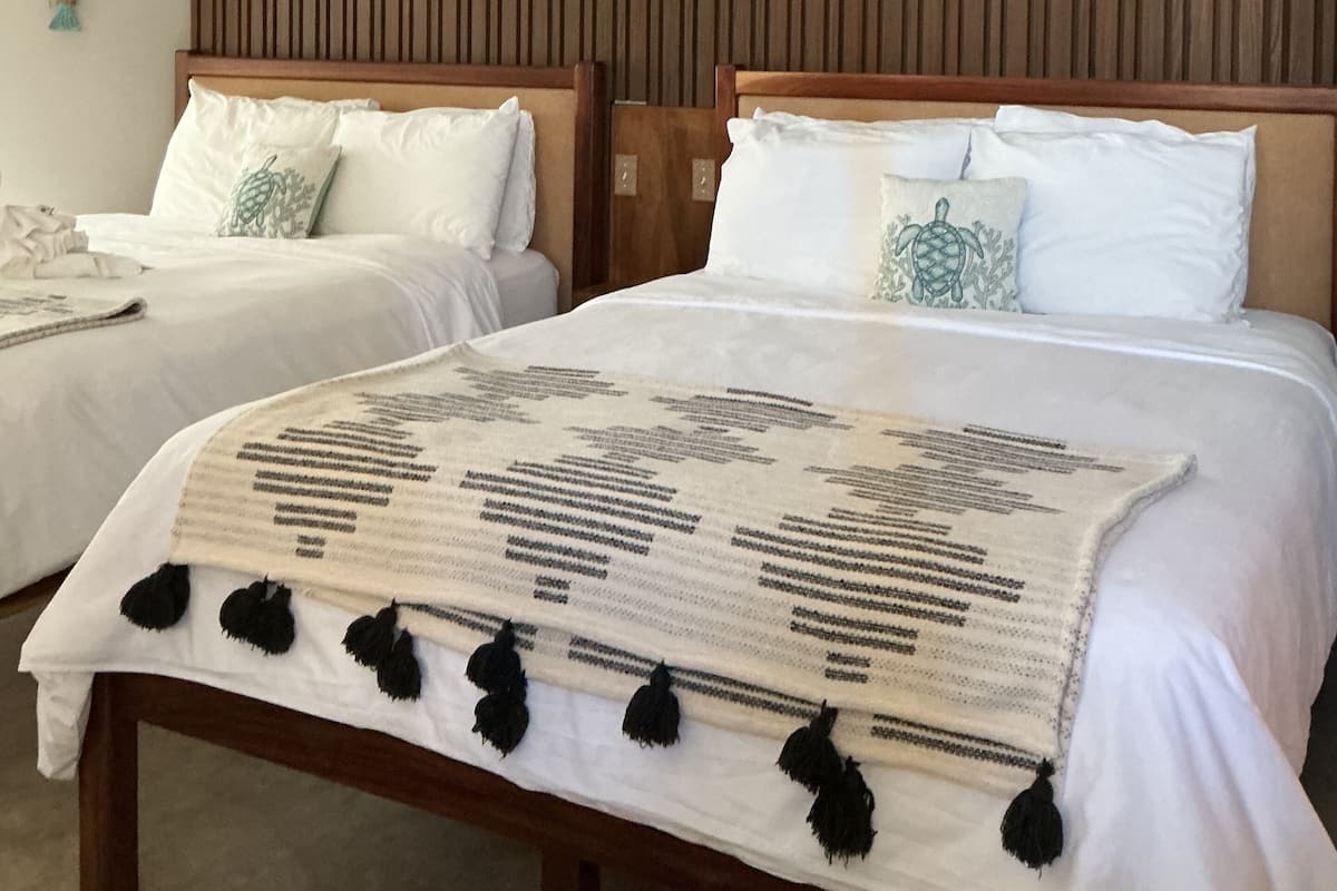 Habitación de hotel con dos camas, cabeceros de madera y un ventilador de techo.