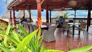 A covered outdoor seating area with wicker furniture, a wooden deck, and a view of the ocean. - Mata Rocks Resort (San Pedro)