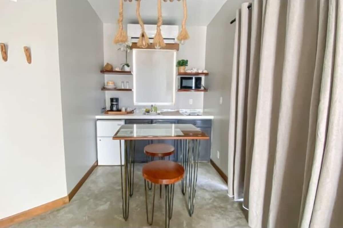 Cocina compacta con una isla central, un refrigerador y un microondas. Hay tres taburetes en la isla y una lámpara colgante arriba.