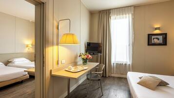 A hotel room with a bed, a desk with a lamp, a TV, and a chair.