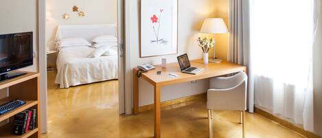 Una habitación de hotel con una cama, un escritorio con una computadora portátil, una silla, un televisor y una estantería.