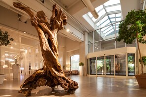 Un vestíbulo amplio con una gran escultura de madera, puertas de cristal que dan a un conservatorio y plantas de interior.