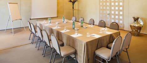 A conference room with a long table, chairs, a projector screen, and a decorative vase.