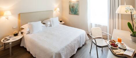 A hotel room with a large bed, bedside tables with lamps, a chair, a tray with breakfast, and a painting on the wall.