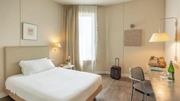 Habitación de hotel con cama, escritorio, silla, lámpara, maleta y bolso de mano.