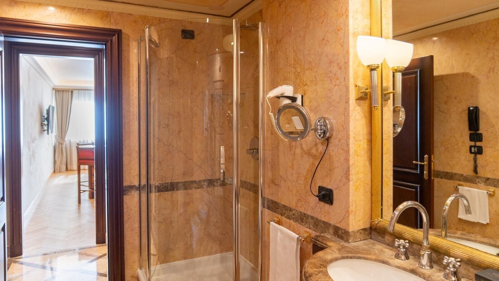 A hotel bathroom with a glass-enclosed shower, a sink with a mirror, and a towel rack.