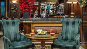 A bar area with two velvet armchairs, a round table, a bar counter with a wine cooler, and a Christmas wreath on the wall. - River Château Hotel (Rome)