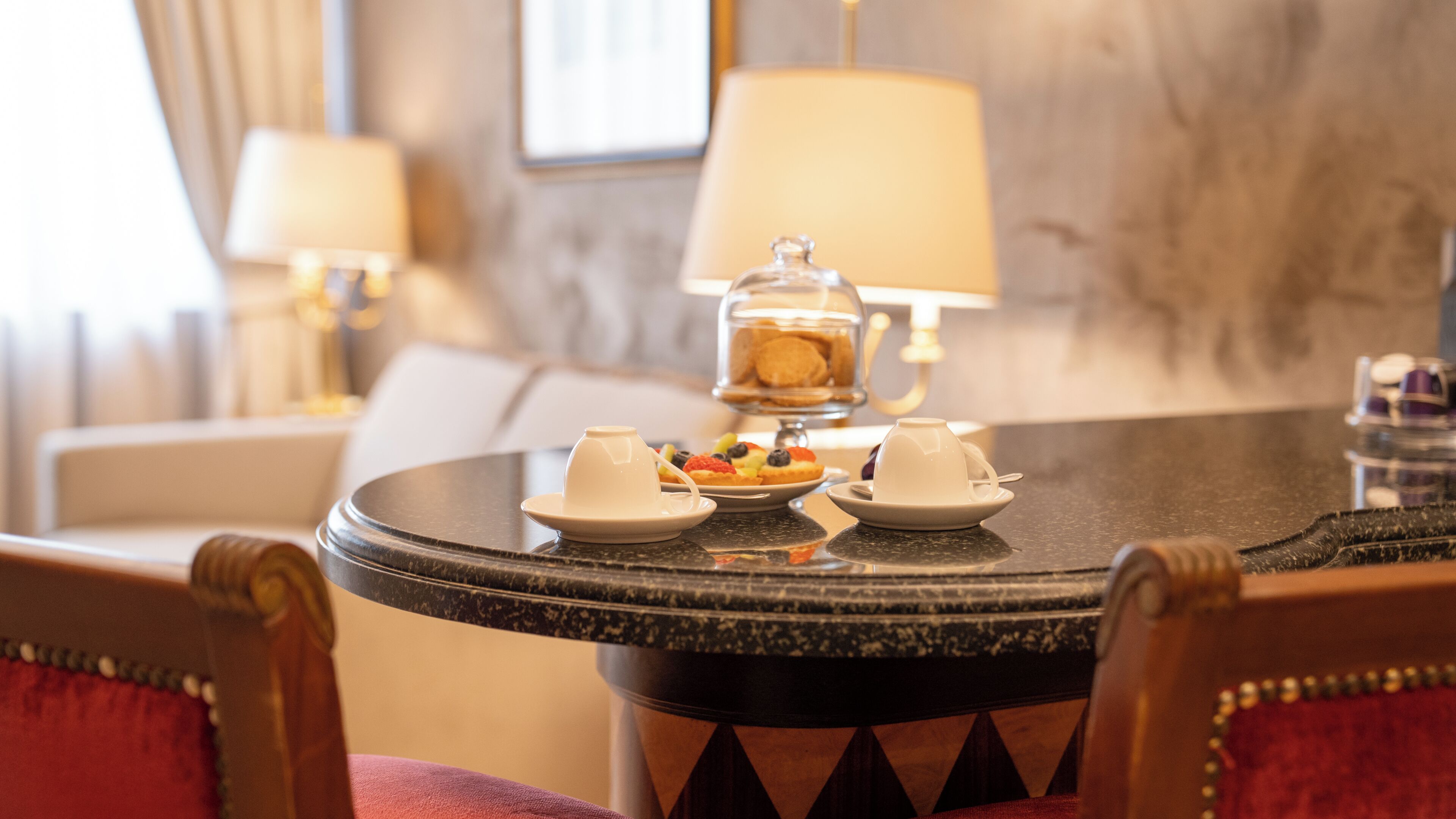 A dining area with a round table, chairs, a lamp, and a glass container with food.
