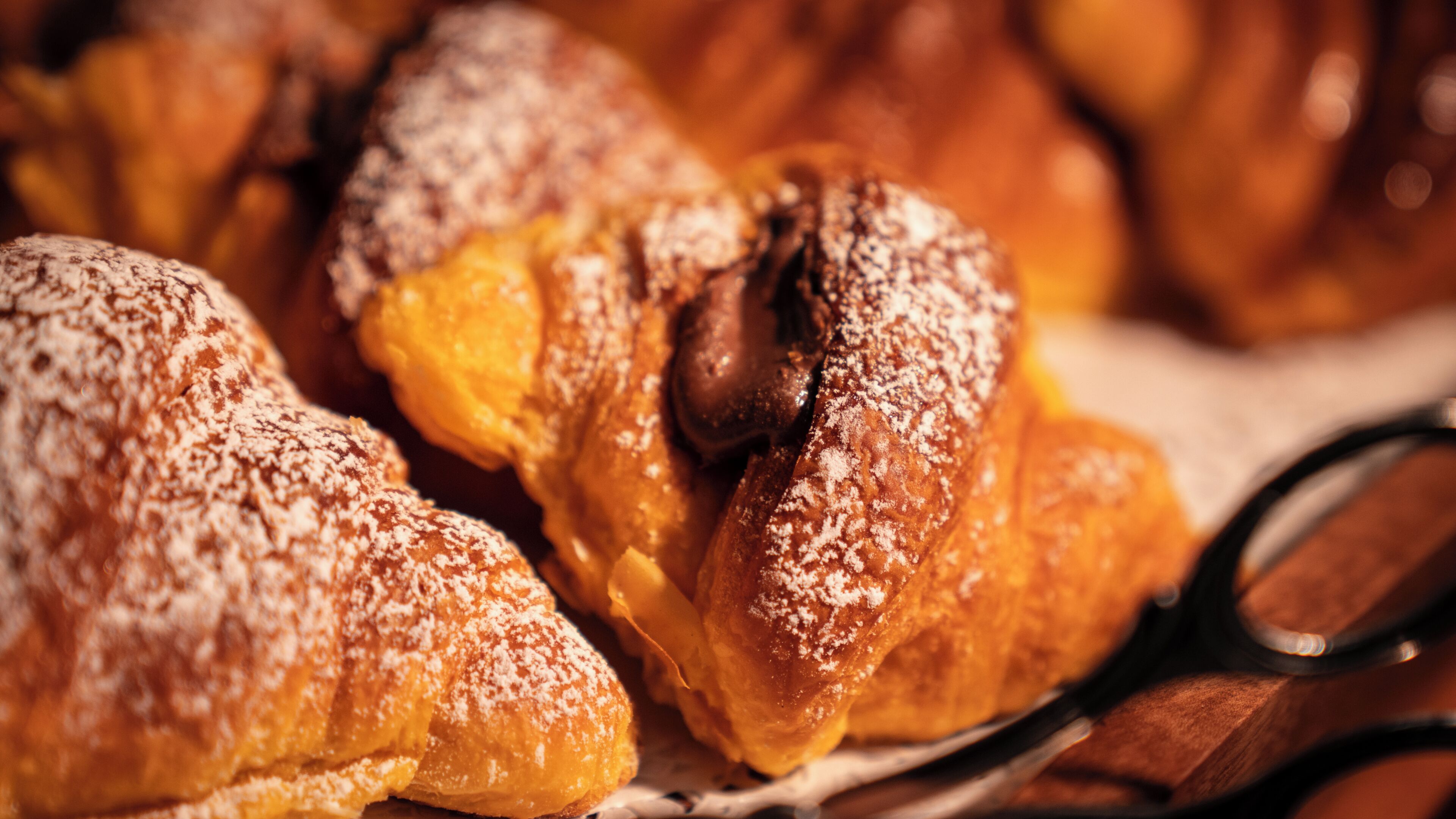 A close-up of pastries with powdered sugar, a pair of scissors, and a wooden surface.