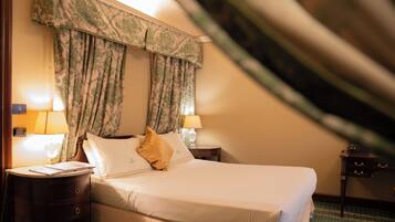 Una habitación de hotel con cama, dos lámparas de noche, una mesita de noche y una ventana con cortinas.