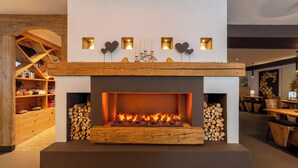 A modern fireplace with a wooden mantel, flanked by stacks of firewood. - Hotel Faloria (Moena)