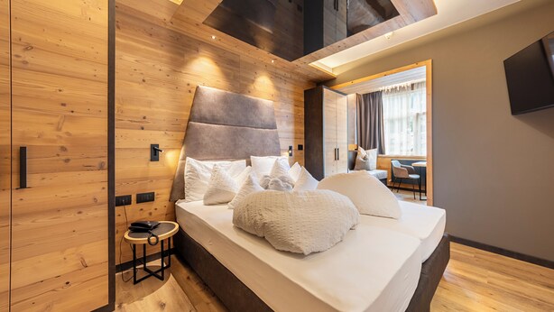 A modern bedroom with a wooden ceiling, a large bed with white bedding, and a small bedside table with a telephone. - Hotel Faloria (Moena)