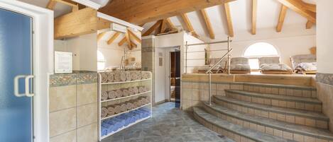 A spa area with stone-tiled floors, wooden beams, a staircase, and shelves with towels.