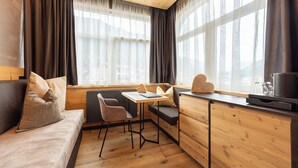 A cozy cabin-style room with a wooden ceiling, a sofa, a dining table, and a kitchenette. - Hotel Faloria (Moena)