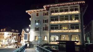 A multi-story hotel with balconies adorned with lights, a visible flag, and a sign indicating a no parking zone. - Hotel Faloria (Moena)