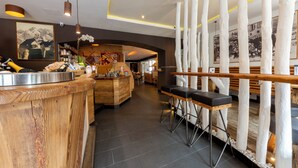 A modern bar area with a wooden counter, bar stools, and a decorative white column structure. - Hotel Faloria (Moena)