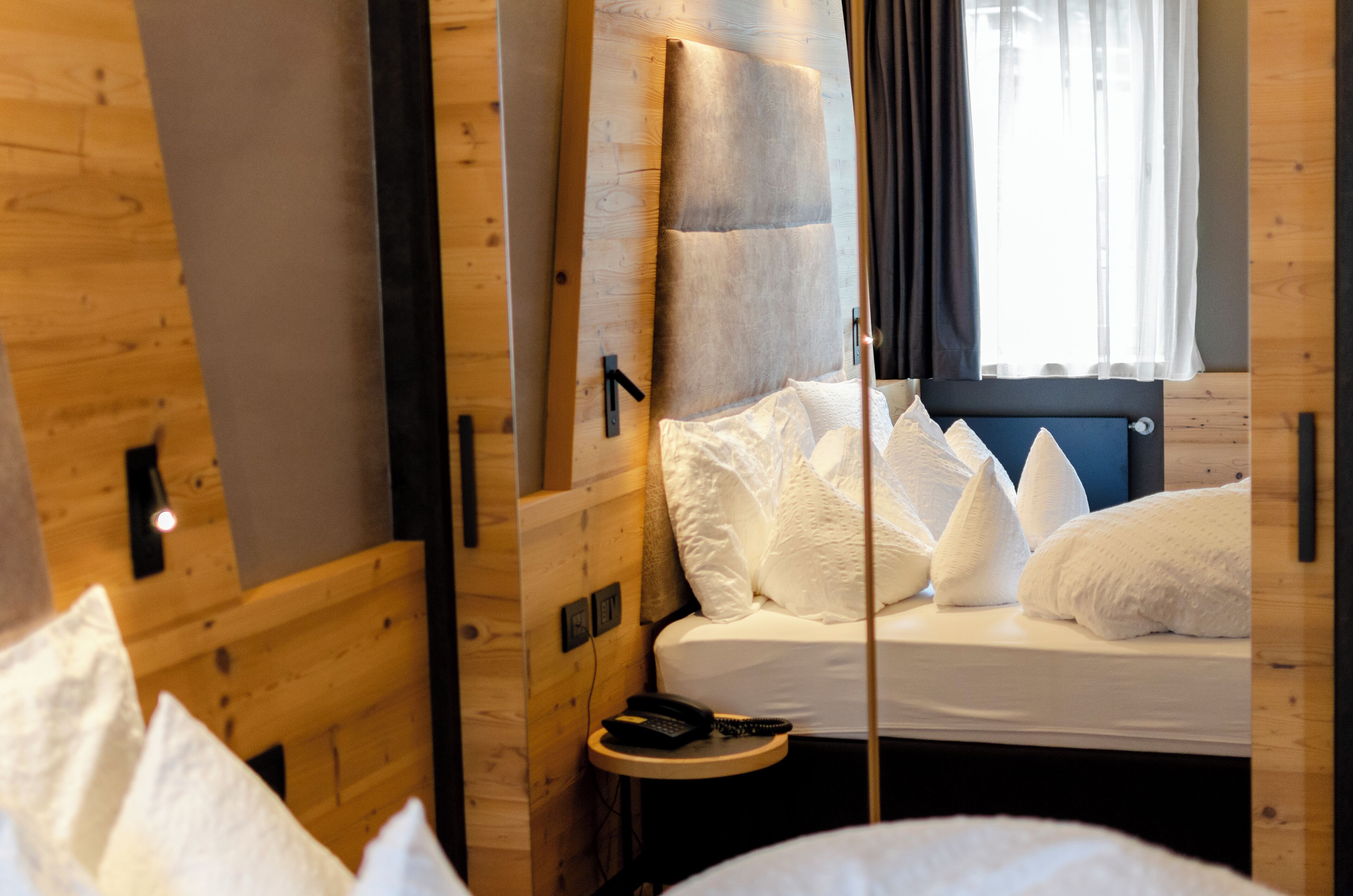 Een kamer met houten vloeren, een bed, een nachtkastje en een raam met gordijnen.
