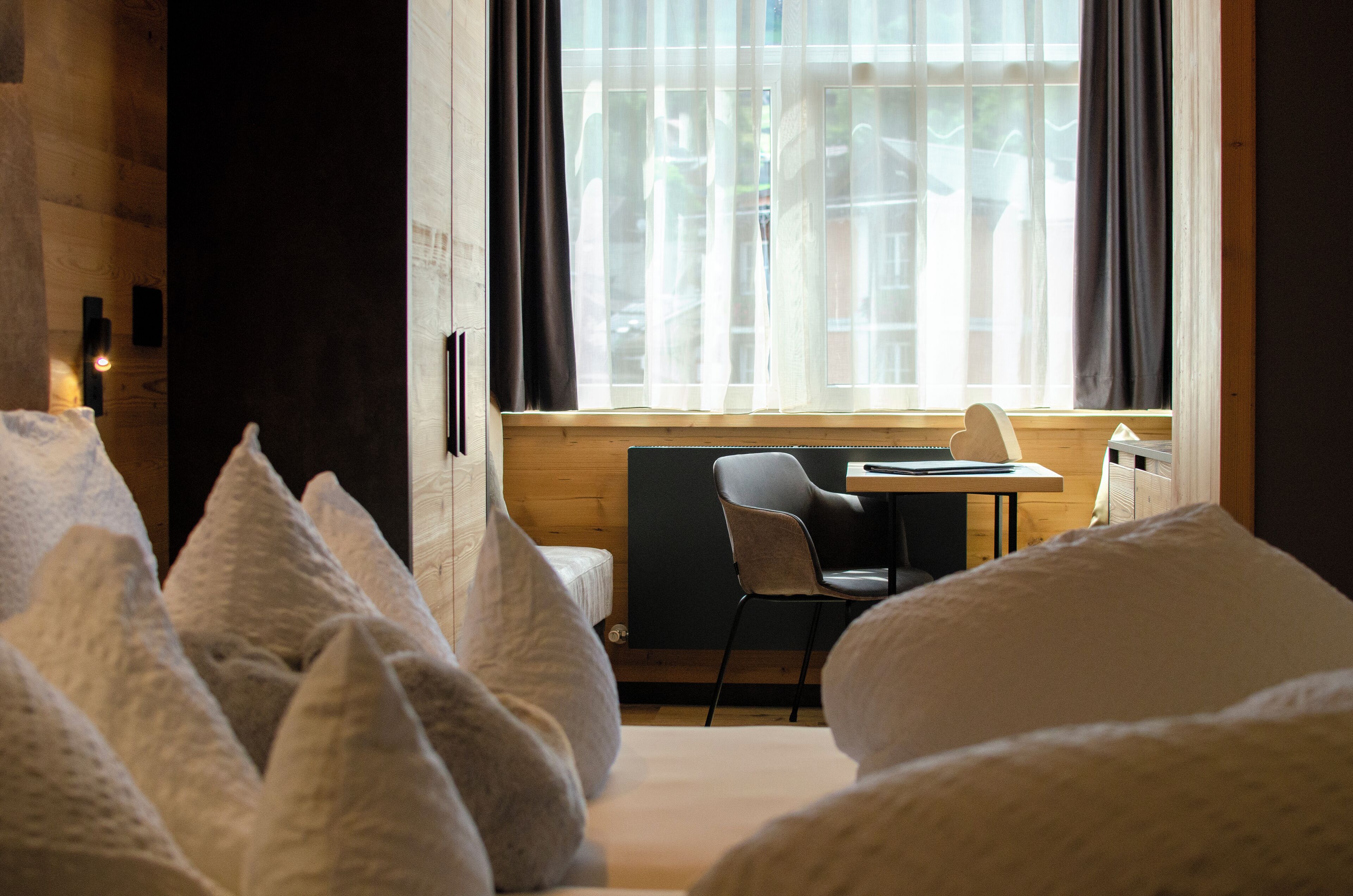 A hotel room with a bed, a chair, a small table, and a window with curtains.