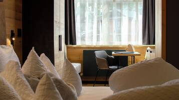 A hotel room with a bed, a chair, a small table, and a window with curtains.