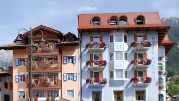 Ein Hotel mit mehreren Balkonen, die mit Blumen geschmückt sind, im traditionellen alpinen Baustil und mit einer Bergkulisse.