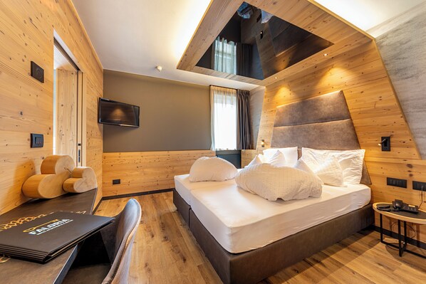 Un dormitorio moderno con techo inclinado, cama con ropa blanca, televisor de pantalla plana y cabecera de madera.