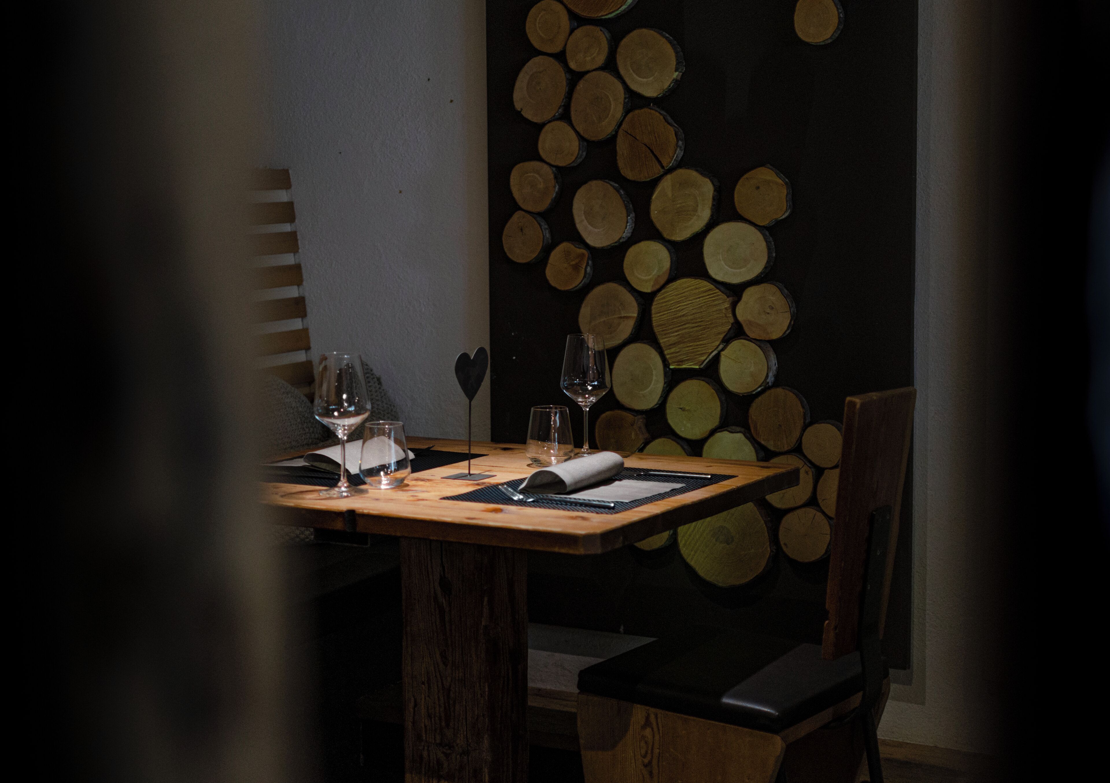 A dining table with a wooden top, two wine glasses, a rolled napkin, and a menu.