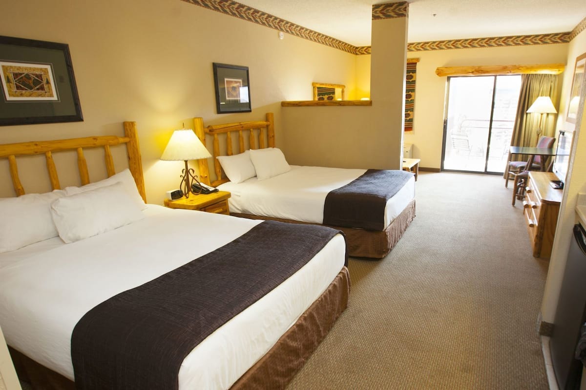 Een hotelkamer met twee bedden, een bureau, een stoel, een lamp en een groot raam.