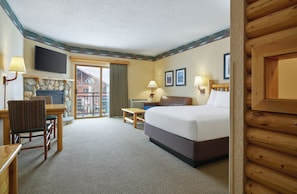 A hotel room with a bed, a desk, a chair, a fireplace, a television, and a balcony.