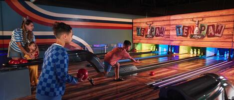 Une salle de bowling avec plusieurs pistes, un panneau en bois indiquant l’entrée, et un mur coloré orné d’un motif ondulé.