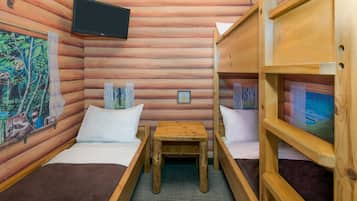 A cabin with two wooden bunk beds, a small wooden table, and a mounted television.