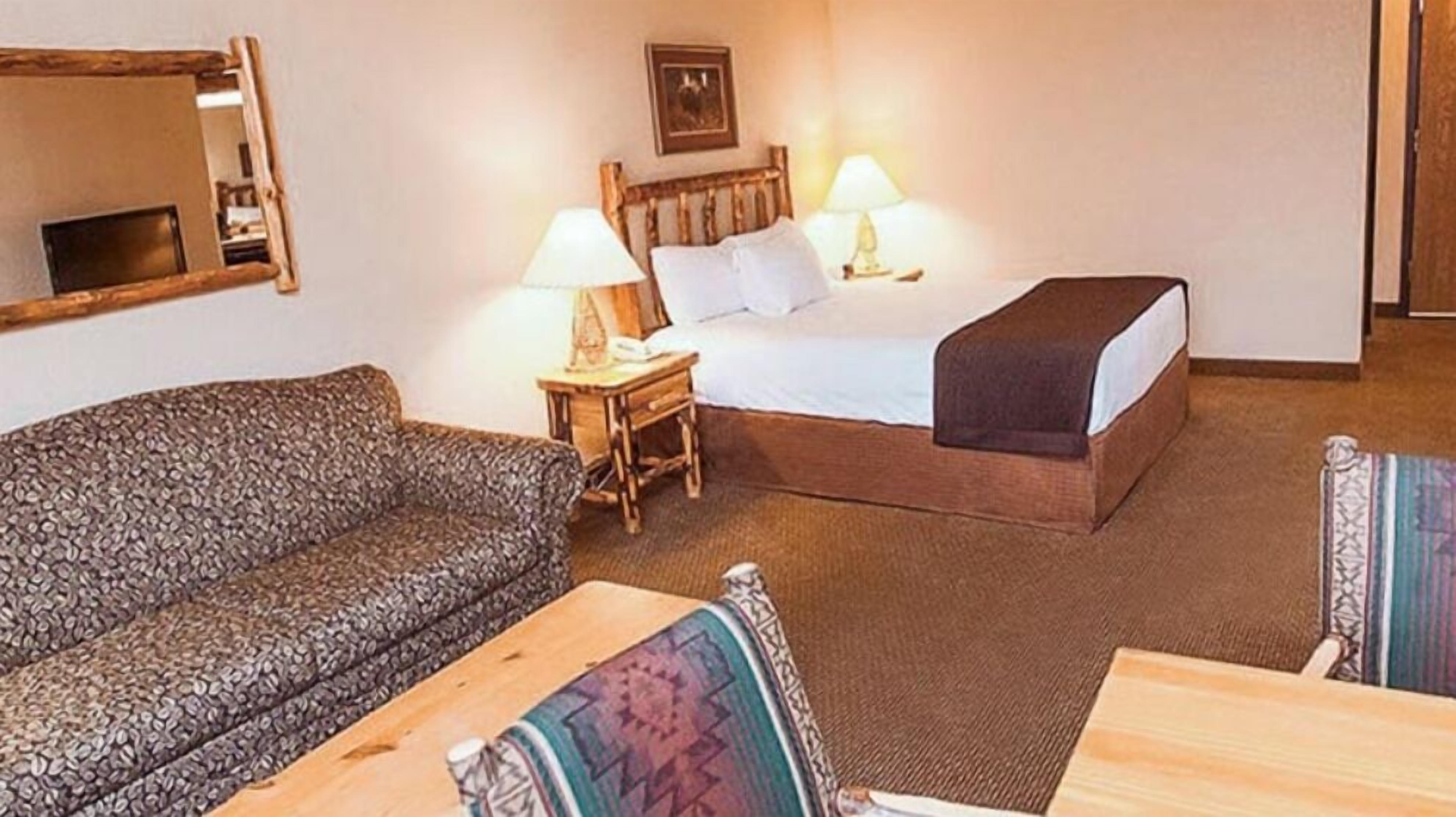 A hotel room with a bed, a sofa, a small table, and a nightstand with lamps.
