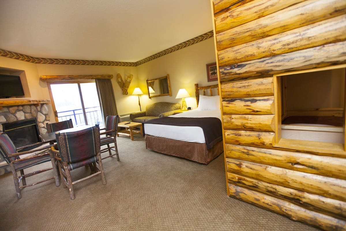Een hotelkamer met een stenen openhaard, een bed, een bureau met stoel, een raam met gordijnen en een houten wand.
