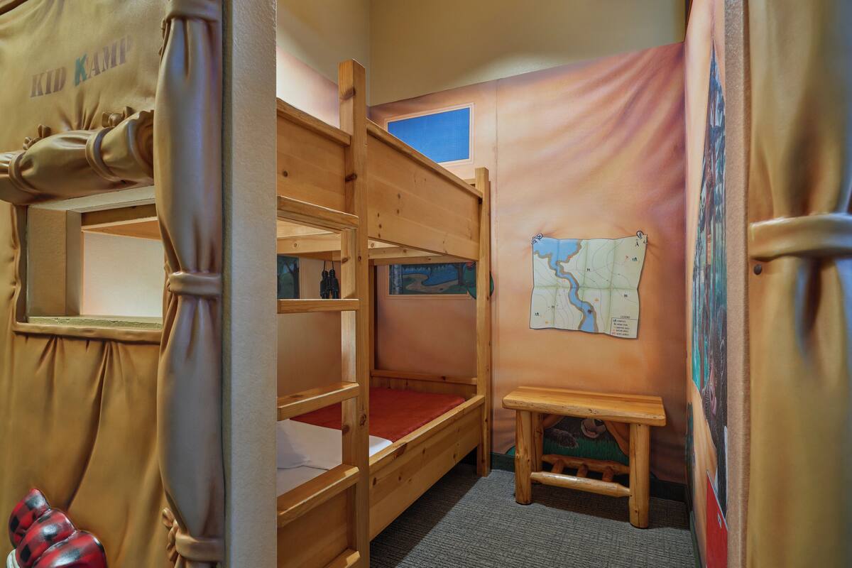 Een slaapkamer met een stapelbed, een kaart aan de muur, een tafeltje en een raam.