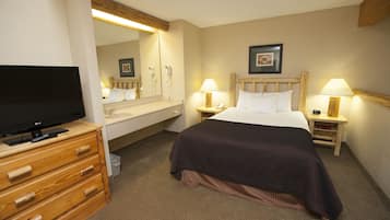 Une chambre d’hôtel avec un lit, des tables de chevet avec des lampes, un téléviseur posé sur une commode en bois, un miroir et un tableau encadré accroché au mur.