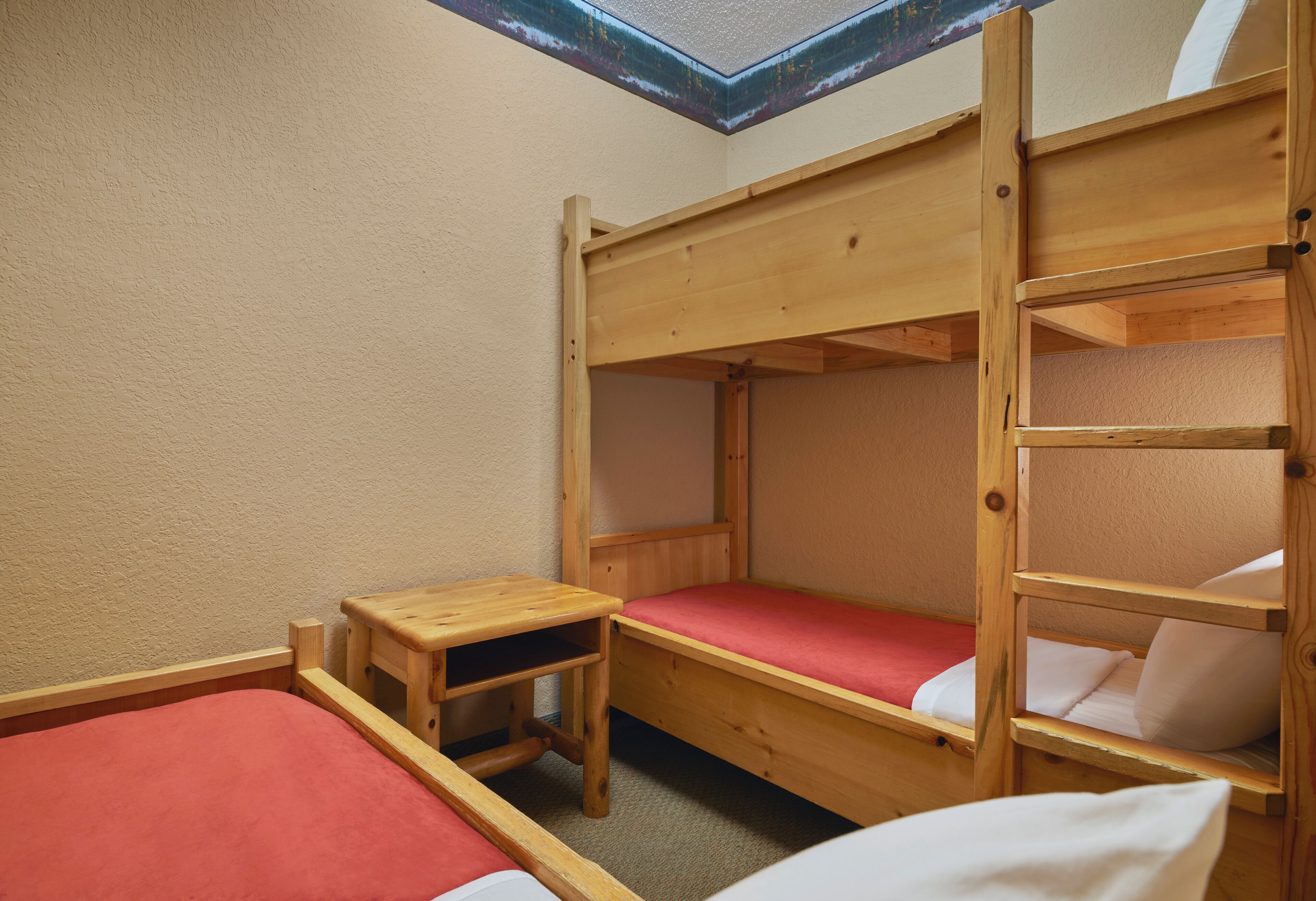 Une chambre avec un lit superposé, une lucarne, une petite table en bois et une couverture rouge.